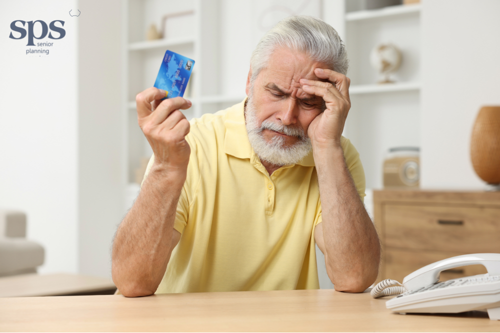 Senior man looking worried while holding his credit card, realizing he may have been scammed; assistance available through Senior Planning Services.
