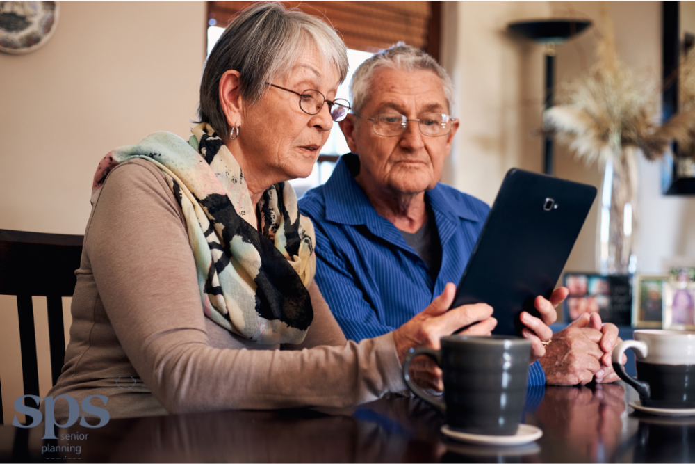 Two seniors reviewing income on a tablet device, getting support from Senior Planning Services to manage Medicaid planning.