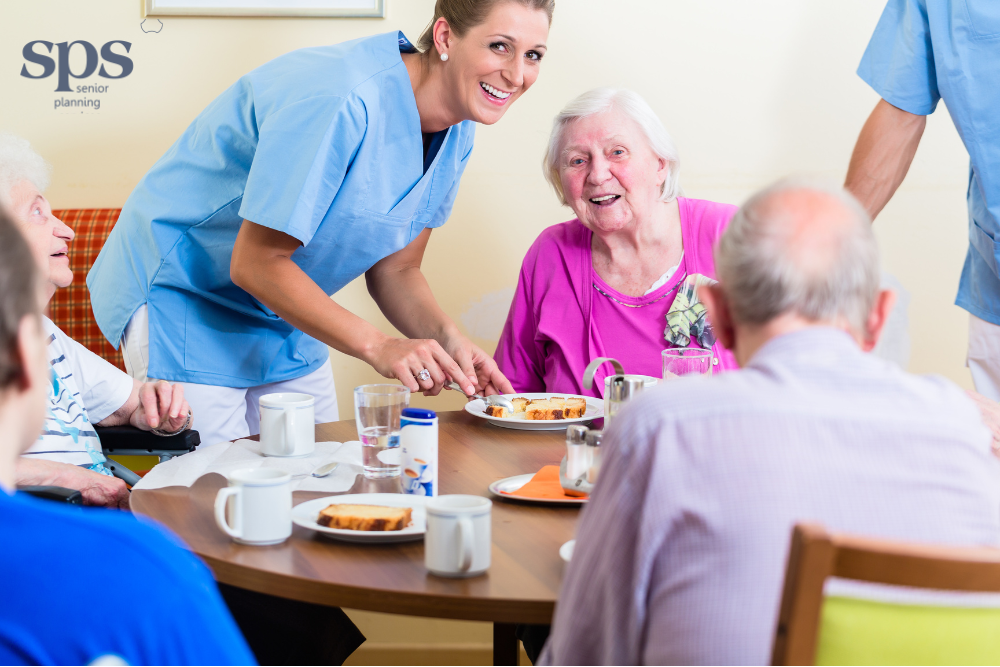 Smiling caregiver leaning toward an elderly woman at a table in a nursing home, representing compassionate care and senior planning services.